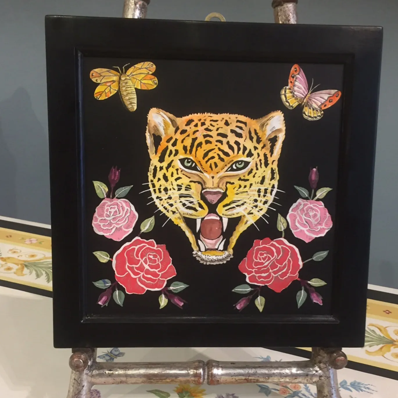 Scagliola dipinge un felino con fiori e insetti